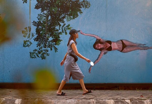 Jeune femme portant une visière de protection devant une fresque représentant une femme en bikini, Jakarta - Sputnik Afrique