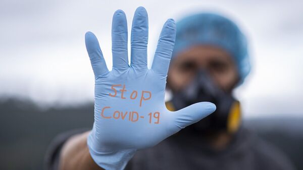 Un homme équipé d'un gant où est inscrit la mention Stop Covid-19 - Sputnik Afrique