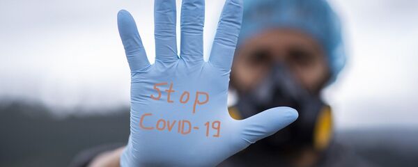 Un homme équipé d'un gant où est inscrit la mention Stop Covid-19 - Sputnik Afrique