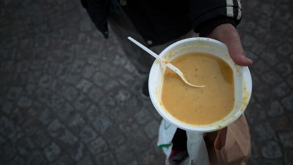Un individu tient un bol de soupe lors d'une distribution du Secours Populaire - Sputnik Afrique
