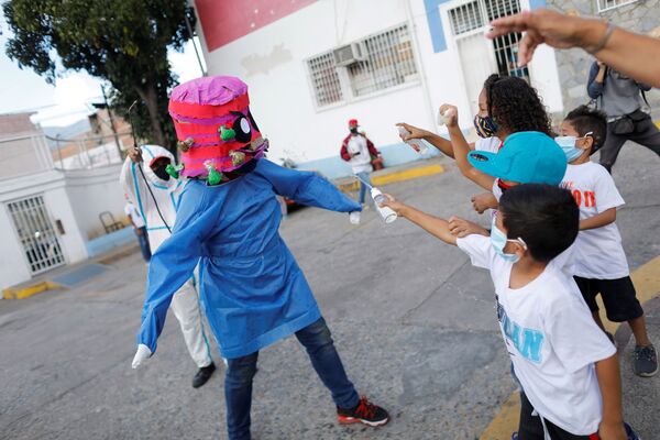 Des enfants jettent de l'alcool et du gel désinfectant sur une personne qui porte un masque représentant le Covid-19 lors de l'incendie traditionnel de Judas dans le cadre des célébrations de la Semaine Sainte, dans le quartier de Cementerio, à Caracas, Venezuela, le 4 avril 2021. - Sputnik Afrique