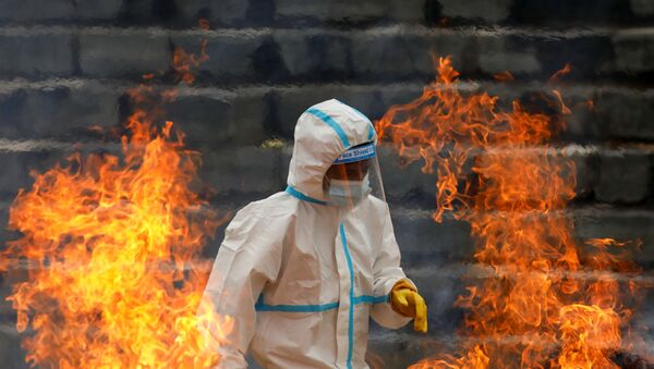 A man wearing personal protective equipment (PPE) walks past the fire as he cremates the bodies of people who died due to coronavirus disease (COVID-19), as India's outbreak spreads across South Asia, in Kathmandu, Nepal May 5, 2021.  - Sputnik Afrique