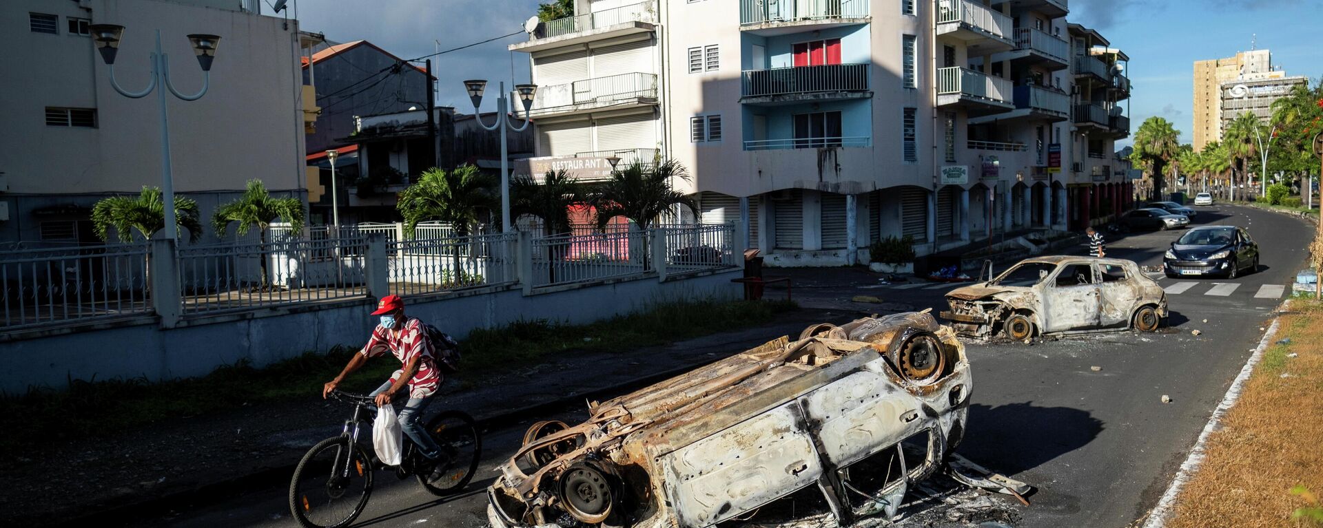 Un homme passe devant des voitures incendiées après de violentes manifestations qui ont éclaté contre les restrictions du COVID-19, à Pointe-à-Pitre, en Guadeloupe, le 21 novembre 2021.  - Sputnik Afrique, 1920, 23.11.2021