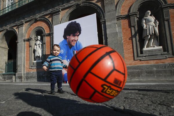 Le stade du club de football de Naples porte désormais le nom de Diego Maradona: le footballeur argentin a fait de ce club autrefois très moyen l’un des plus forts d’Europe.Sur la photo: un enfant avec un ballon devant une photo de Diego Maradona sur la Piazza del Plebiscito à Naples, en Italie. - Sputnik Afrique
