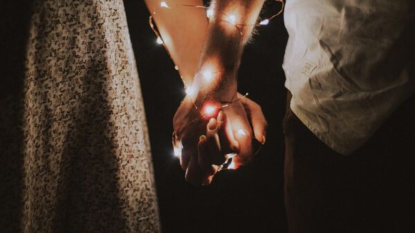 Homme et femme tenant les uns les autres à la main avec des guirlandes lumineuses - Sputnik Afrique