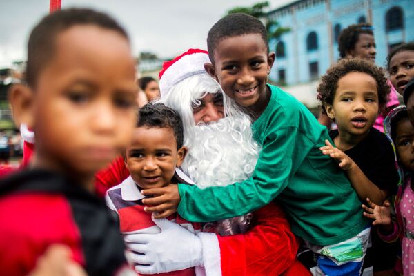 L’une des traditions populaires chez les chrétiens occidentaux la veille de Noël consiste à laisser une place à la table de fête pour un éventuel hôte.Sur la photo: un homme déguisé en père Noël avec ses enfants lors de la distribution de repas gratuits dans une favela de Rio de Janeiro. - Sputnik Afrique