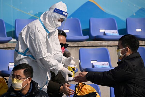 Un membre du personnel asperge les mains des spectateurs avec une solution désinfectante au stade Big Air Shougang, à Pékin. - Sputnik Afrique