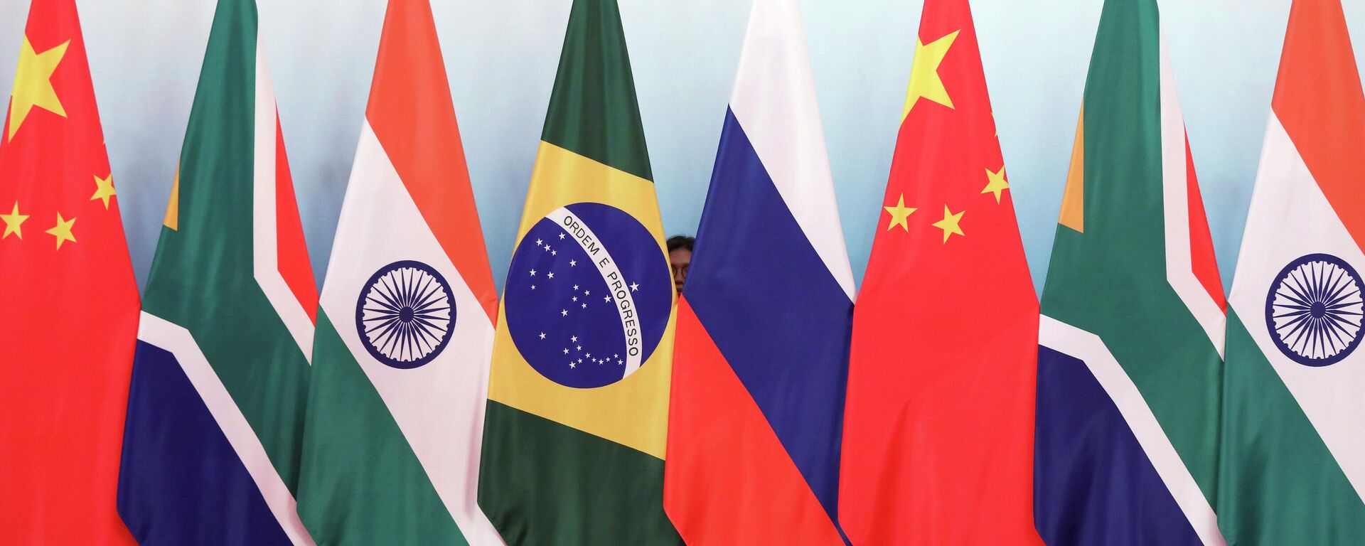 Staff worker stands behind national flags of Brazil, Russia, China, South Africa and India to tidy the flags ahead of a group photo during the BRICS Summit at the Xiamen International Conference and Exhibition Center in Xiamen, southeastern China's Fujian Province, Monday, Sept. 4, 2017. - Sputnik Africa, 1920, 23.07.2023