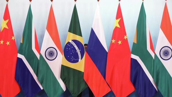 Staff worker stands behind national flags of Brazil, Russia, China, South Africa and India to tidy the flags ahead of a group photo during the BRICS Summit at the Xiamen International Conference and Exhibition Center in Xiamen, southeastern China's Fujian Province, Monday, Sept. 4, 2017. - Sputnik Africa