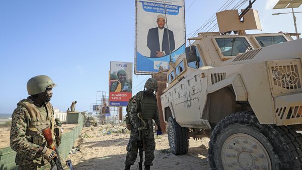 Ugandan peacekeepers with the African Transition Mission in Somalia (ATMIS) stand next to their armored vehicle, with a campaign poster for presidential candidate Ahmed Abdullahi Samow seen above, on a street in Mogadishu, Somalia Tuesday, May 10, 2022 - Sputnik Africa