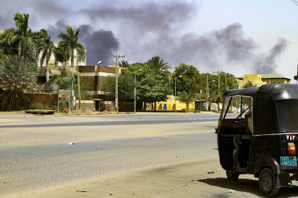 Smoke rises from buildings as a tuktuk taxi driver sits in his vehicle along a deserted street in Sudan&#x27;s capital on April 16, 2023. - Sputnik Africa