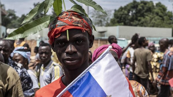A demonstrator with foliage on to his head, a sign of compassion in Central African Republic, holds a Russian flag with the emblem of Russia on while posing for a portrait in Bangui, on March 22, 2023 during a march in support of Russia and China's presence in the Central African Republic. - Sputnik Africa