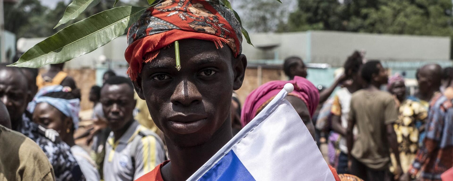 A demonstrator with foliage on to his head, a sign of compassion in Central African Republic, holds a Russian flag with the emblem of Russia on while posing for a portrait in Bangui, on March 22, 2023 during a march in support of Russia and China's presence in the Central African Republic. - Sputnik Africa, 1920, 19.04.2023