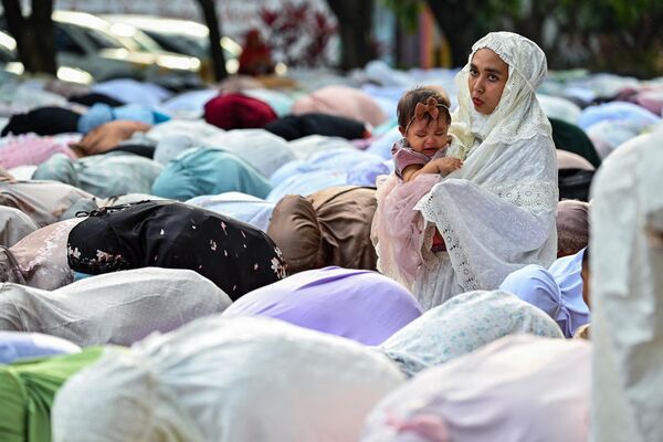 A woman in the congregation tends to a child as Muslims take part in a morning prayer celebrating Eid al-Fitr. - Sputnik Africa