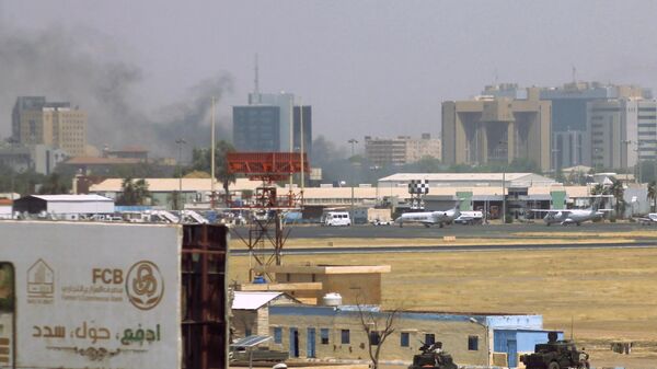 Military vehicles can be seen as smoke billows above buildings in the vicinity of the Khartoum airport on April 15, 2023, amid clashes in the city. - Sputnik Africa