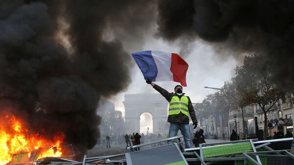 In this Nov. 24, 2018 file photo, a demonstrator waves the French flag on a burning barricade on the Champs-Elysees avenue with the Arc de Triomphe in background, during a demonstration against the rise of fuel taxes.  - Sputnik Africa