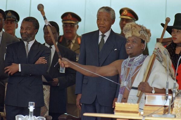 A Praise singer, dressed in native costume and wielding a ceremonial cane, sings praises as Nelson Mandela stands behind him at the starts of the Presidential Inauguration ceremony in Pretoria, May 10, 1994. - Sputnik Africa