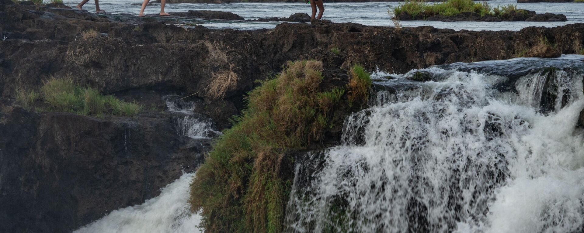 A tourist walks with guides at the Zambezi river at the edge of the Victoria Falls, in Victoria Falls, on December 10, 2019 - Sputnik Africa, 1920, 28.05.2023