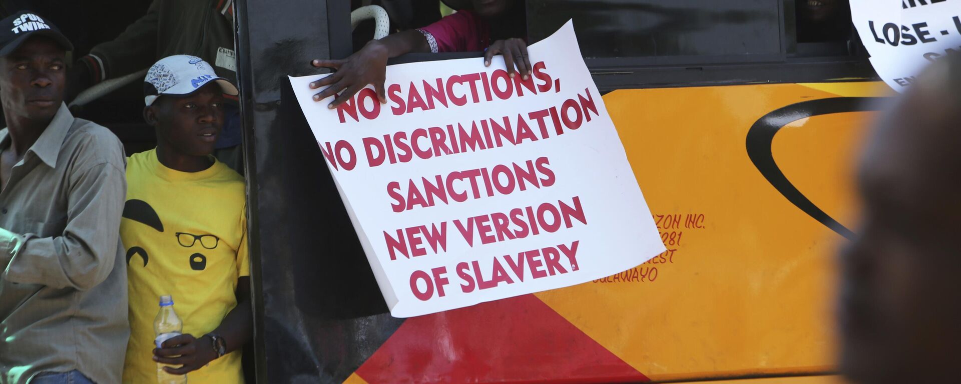 A woman on a bus holds a placard while protesting over U.S. sanctions that the Zimbabwean government blames for the country's worsening economic problems, in Harare, Friday, Oct, 25, 2019. The Zimbabwe government blames U.S. sanctions for devastating economic conditions, galloping inflation and severe shortages of basic goods, but the U.S. blames corruption, financial mismanagement and human rights violations instead - Sputnik Africa, 1920, 31.05.2023