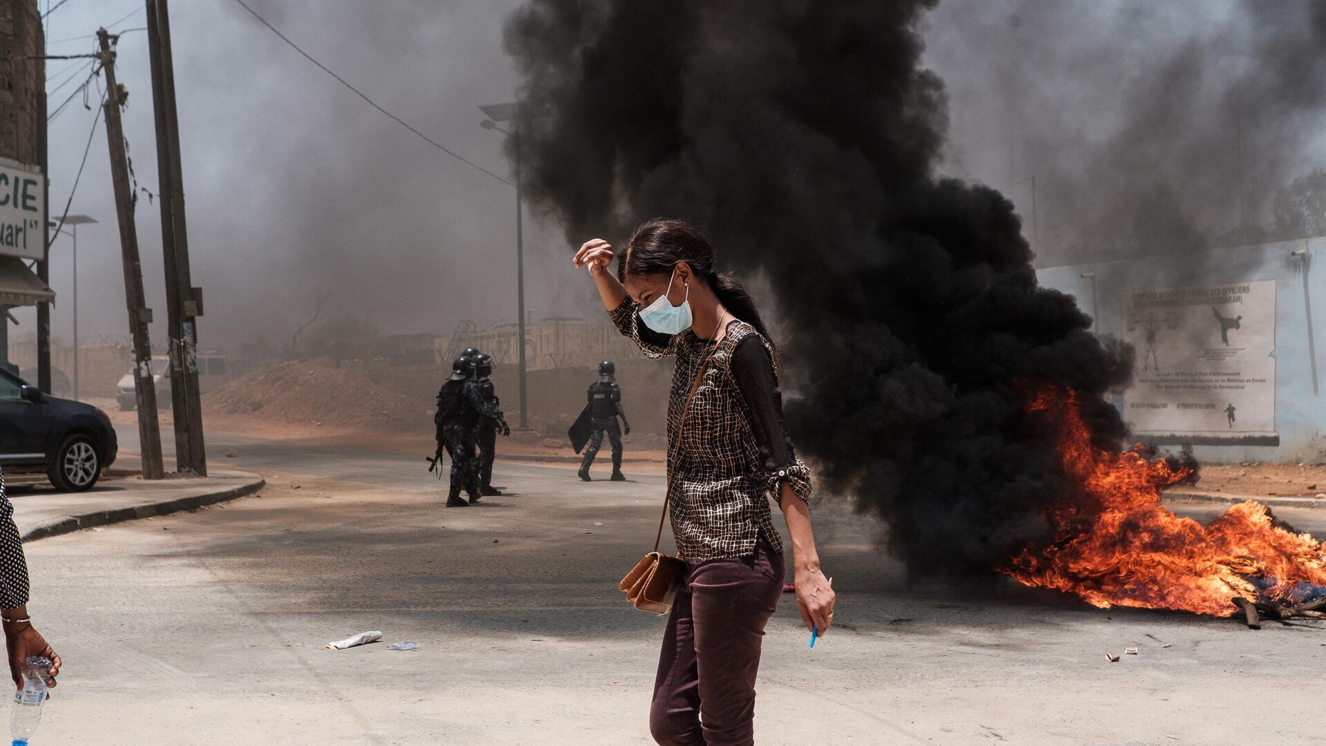 A women walks past a burning fire near police in Dakar on June 1, 2023, during unrest following the sentence of opponent Ousmane Sonko. A court in Senegal on Thursday sentenced opposition leader Ousmane Sonko, a candidate in the 2024 presidential election, to two years in prison on charges of corrupting youth but acquitted him of rape and issuing death threats. - Sputnik Africa, 1920, 02.06.2023