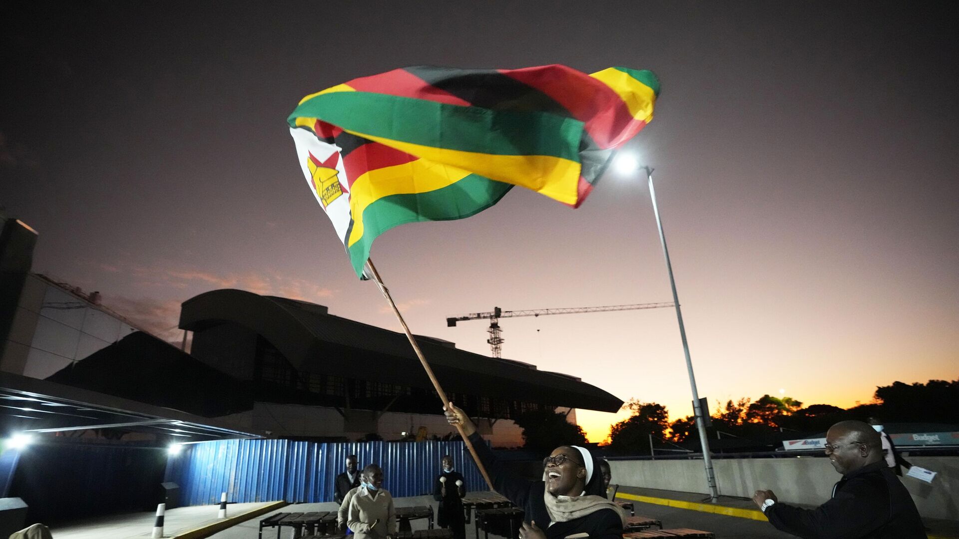 A nun celebrates while holding a Zimbabwean flag to welcome the Zimbabwean high school World and European moot court competition champions as they arrive back at the Robert Mugabe International airport in Harare, Thursday,  July, 7, 2022.  - Sputnik Africa, 1920, 04.07.2023