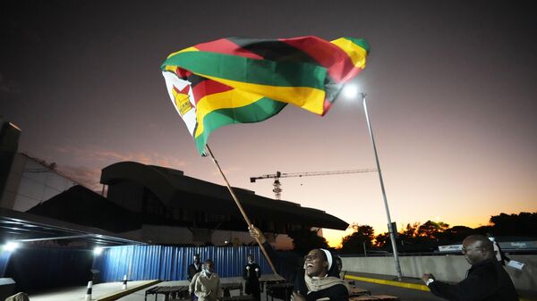 A nun celebrates while holding a Zimbabwean flag to welcome the Zimbabwean high school World and European moot court competition champions as they arrive back at the Robert Mugabe International airport in Harare, Thursday,  July, 7, 2022.  - Sputnik Africa