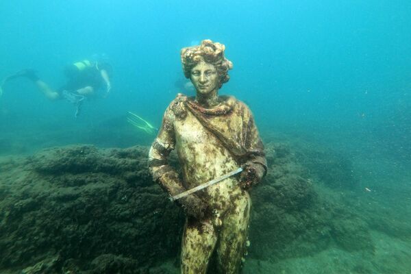 In this photograph taken on August 18, 2021 a dive guide shows tourists a copy of the original statue preserved at the Museum of Baiae, representing Dionysus with ivy crown in the Nymphaeum of punta Epitaffio, the submerged ancient Roman city of Baiae at the Baiae Underwater Park, part of the Campi Flegrei Archaeological Park complex site in Pozzuoli near Naples. Statues which once decorated luxury abodes in this beachside resort are now playgrounds for crabs off the coast of Italy, where divers can explore ruins of palaces and domed bathhouses built for emperors.  - Sputnik Africa