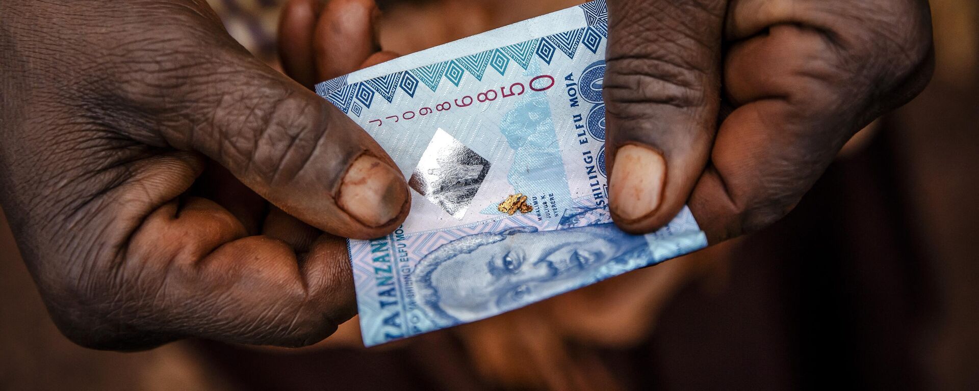 Tanzanian miner Lolesia Limbe folds in a Tanzanian note grains of gold obtained after panning near an open-pit gold mine in Nyarugusu, Geita Region, Tanzania on May 27, 2022. - Sputnik Africa, 1920, 22.06.2023