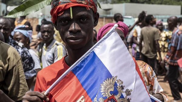 A demonstrator with foliage on to his head, a sign of compassion in Central African Republic, holds a Russian flag with the emblem of Russia on while posing for a portrait in Bangui, on March 22, 2023 during a march in support of Russia and China's presence in the Central African Republic - Sputnik Africa