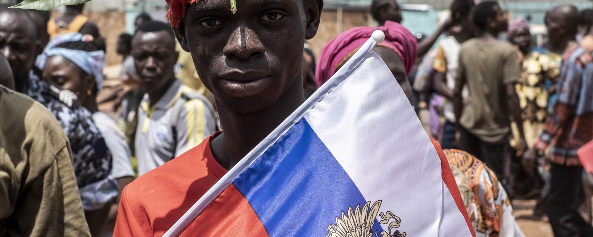 A demonstrator with foliage on to his head, a sign of compassion in Central African Republic, holds a Russian flag with the emblem of Russia on while posing for a portrait in Bangui, on March 22, 2023 during a march in support of Russia and China's presence in the Central African Republic - Sputnik Africa, 1920, 28.06.2023