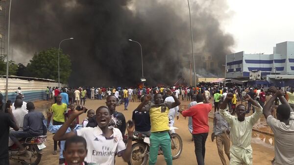 With the headquarters of the ruling party burning in the back, supporters of mutinous soldiers demonstrate in Niamey, Niger - Sputnik Africa