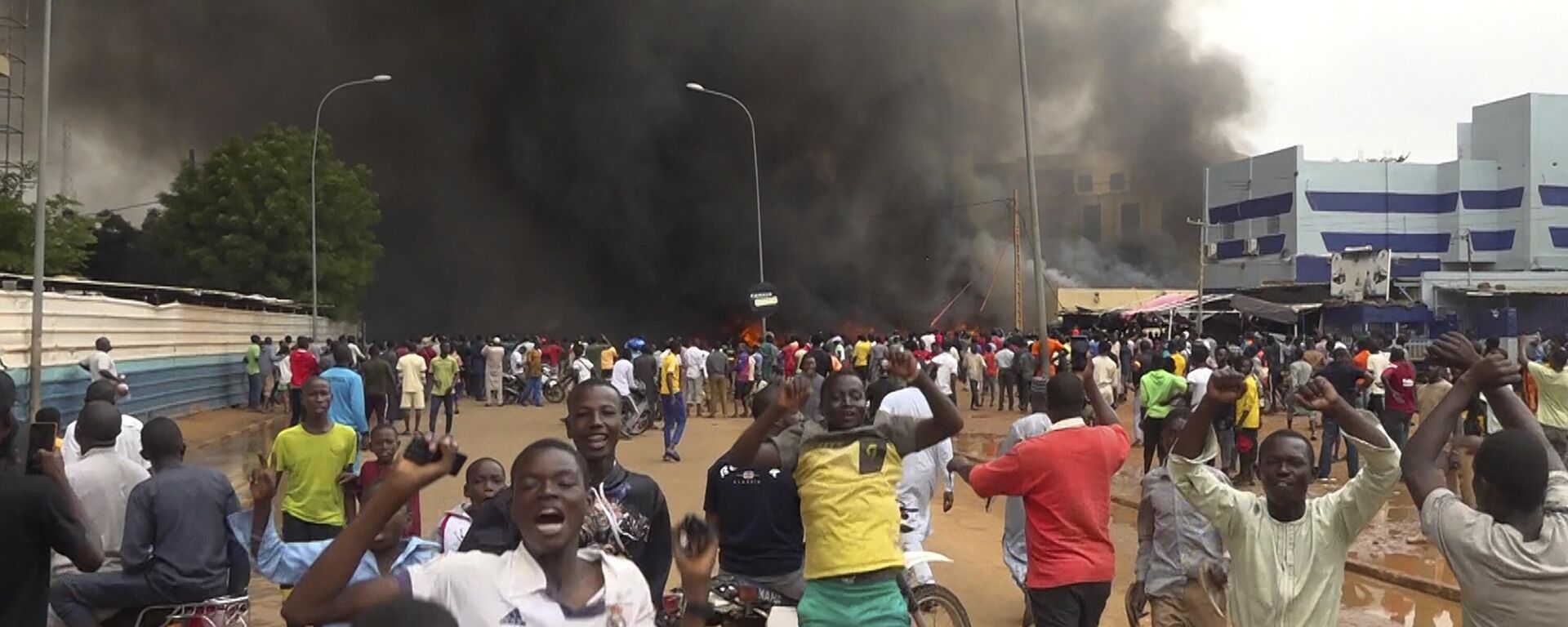 With the headquarters of the ruling party burning in the back, supporters of mutinous soldiers demonstrate in Niamey, Niger - Sputnik Africa, 1920, 02.08.2023