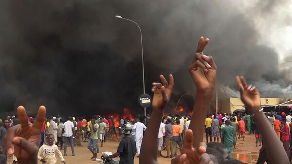 With the headquarters of the ruling party burning in the back, supporters of mutinous soldiers demonstrate in Niamey, Niger, Thursday, July 27 2023. - Sputnik Africa
