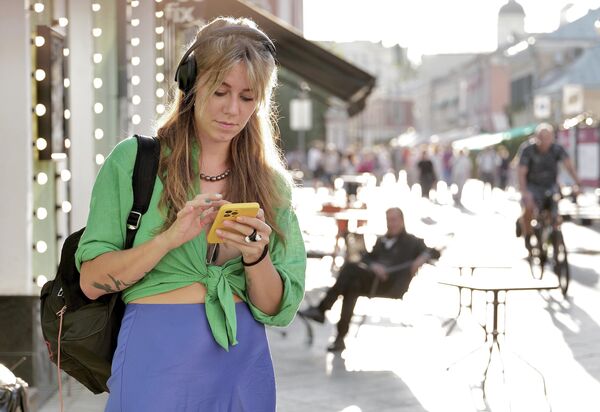 A girl wearing headphones scrolls through her phone on a Moscow street. - Sputnik Africa