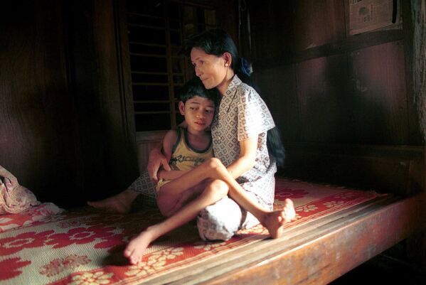 Twelve-year-old Pham Quoc Huy, who is suffering from what his parents say are the effects of the jungle defoliant Agent Orange, is comforted by his mother on a bamboo cot in their home, Feb. 19, 2000. - Sputnik Africa