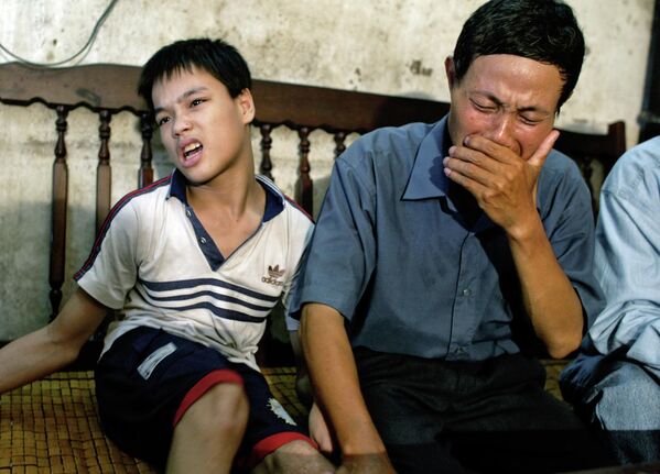 Nguyen Van Quy, 49, weeps while sitting with his son Nguyen Quang Trung, 17, at his house in Hai Phong, Vietnam in July 2004. - Sputnik Africa