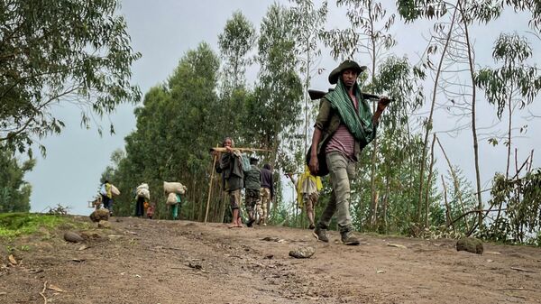 An unidentified armed militia fighter walks down a path as villagers flee with their belongings in the other direction, near the village of Chenna Teklehaymanot, in the Amhara region of northern Ethiopia Thursday, Sept. 9, 2021.  - Sputnik Africa