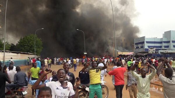 With the headquarters of the ruling party burning in the back, supporters of Niger's ruling junta demonstrate in Niamey, Niger, on July 27, 2023.  - Sputnik Africa