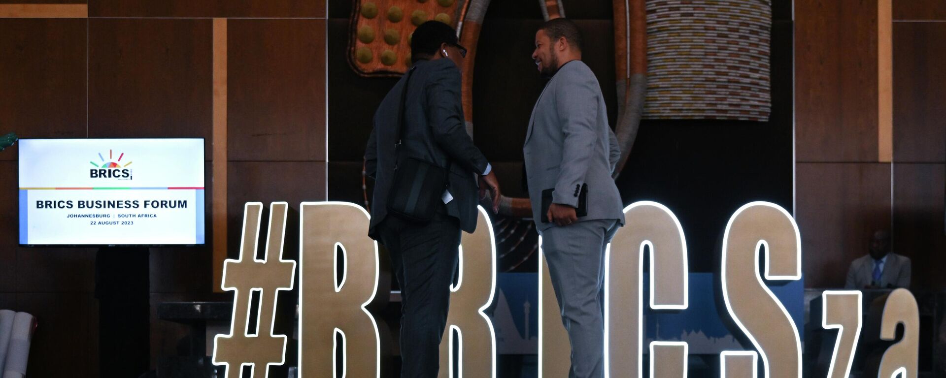 Men stand next to an installation with the logo of BRICS during the 15th BRICS Summit in Johannesburg, South Africa, on Tuesday, August 22, 2023. - Sputnik Africa, 1920, 22.08.2023