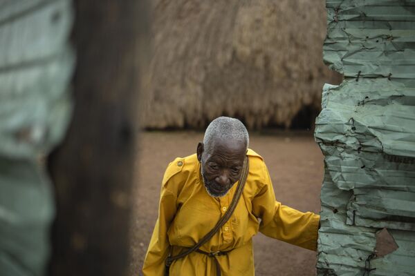 A traditional guard walks past one of the buildings belonging to the Kasubi Royal Tombs in Kampala, Uganda. - Sputnik Africa