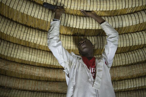 A traditional artisan fixes the circular rings at the ceiling of one of the buildings belonging to the Kasubi Royal Tombs in Kampala. - Sputnik Africa