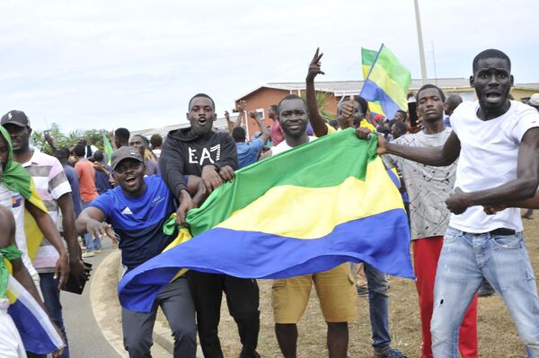 Residents gesture and hold a Gabon national flag as they celebrate in Libreville on August 30, 2023 after a group of Gabonese military officers appeared on television announcing they were &quot;putting an end to the current regime&quot; and scrapping official election results that had handed another term to veteran President Ali Bongo Ondimba. In a pre-dawn address, a group of officers declared &quot;all the institutions of the republic&quot; had been dissolved, the election results cancelled and the borders closed. - Sputnik Africa