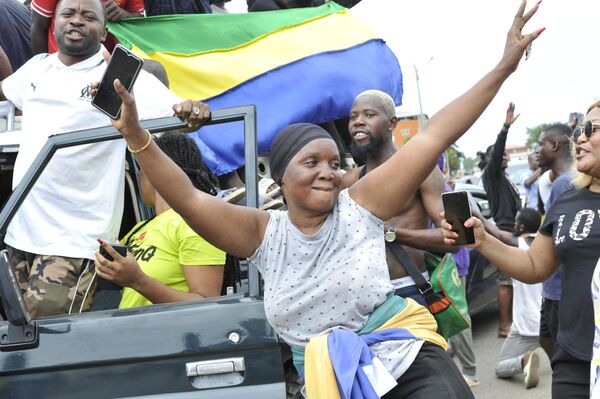 Residents gesture and hold a Gabon national flag as they celebrate in Libreville on August 30, 2023 after a group of Gabonese military officers appeared on television announcing they were &quot;putting an end to the current regime&quot; and scrapping official election results that had handed another term to veteran President Ali Bongo Ondimba. In a pre-dawn address, a group of officers declared &quot;all the institutions of the republic&quot; had been dissolved, the election results cancelled and the borders closed. - Sputnik Africa