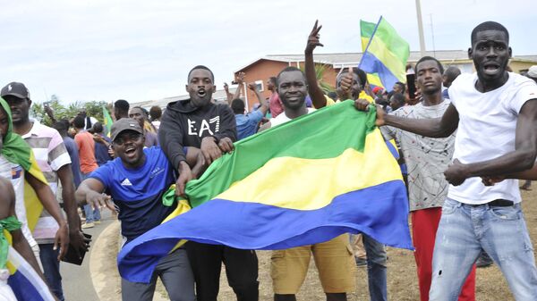 Residents gesture and hold a Gabon national flag in Libreville on August 30, 2023 - Sputnik Africa