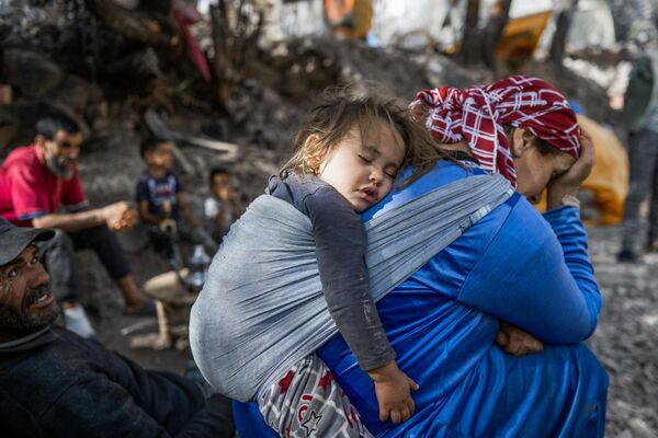 A mother carrying her child on her back rests with others outside their earthquake-damaged house in Tijghicht, in the Atlas Mountains range, on September 14, 2023.  - Sputnik Africa