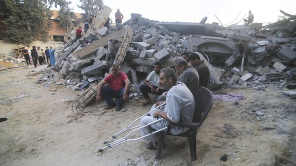 Palestinians sit by the building destroyed in an Israeli airstrike in Rafah, Gaza Strip, Saturday, Oct. 14, 2023.  - Sputnik Africa