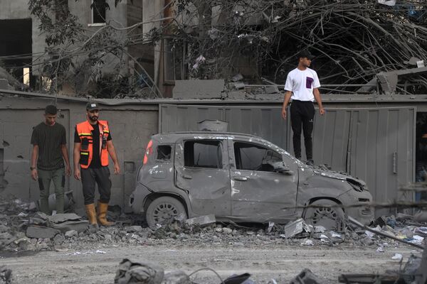 A rescuer and people stand alongside a burnt car following an Israeli strike in Rafah in the southern Gaza Strip, on October 15, 2023.  - Sputnik Africa