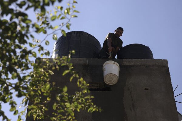 A man lifts a water bucket to the roof to refill a water tank in a house at the Rafah refugee camp, in the southern Gaza Strip on Octobers 15, 2023.  - Sputnik Africa