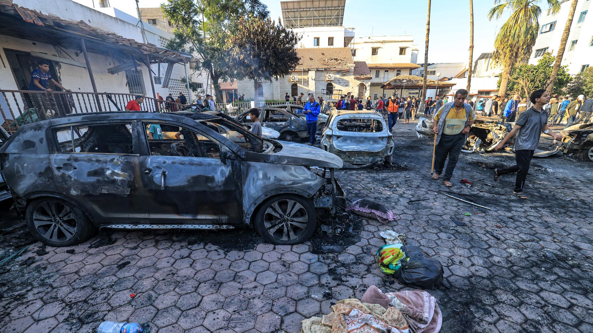 People gather by destroyed vehicles at the site of the Ahli Arab hospital in central Gaza on October 18, 2023 in the aftermath of an overnight blast there.  - Sputnik Africa, 1920, 18.10.2023
