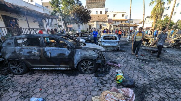 People gather by destroyed vehicles at the site of the Ahli Arab hospital in central Gaza on October 18, 2023 in the aftermath of an overnight blast there.  - Sputnik Africa